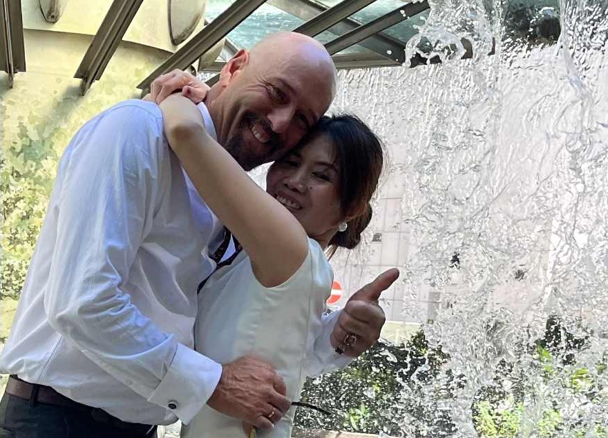 A man gives the thumbs up sign as he hugs his new wife in front of an indoor waterfall