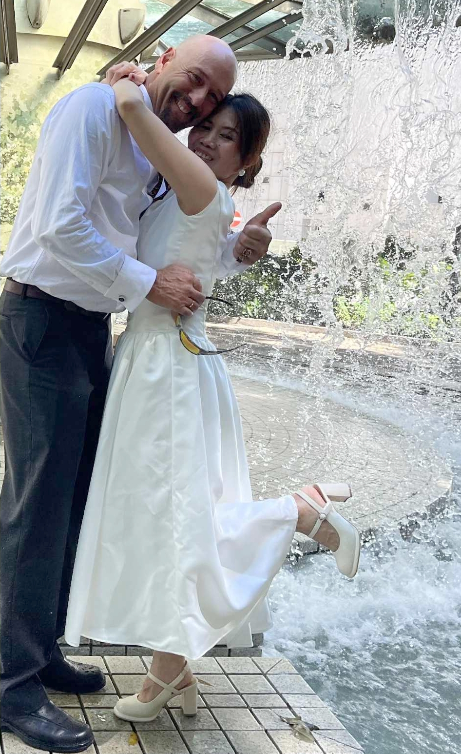 water splashes indoors behind a new bride in white as she hugs her husband