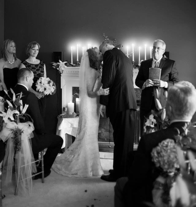 A couple kiss in a small intimate wedding ceremony with lit candles in background