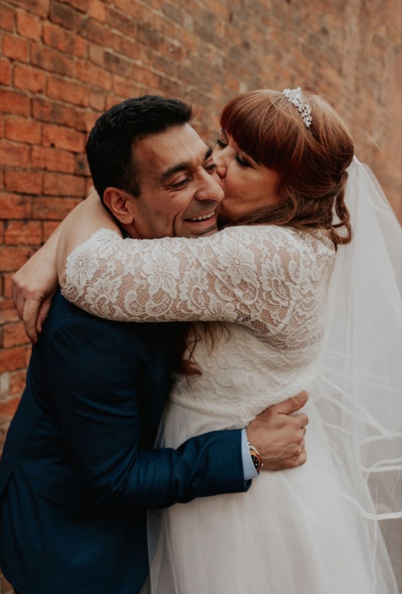 A new bride passionately grabs and kisses her new husband's cheek, as he laughs