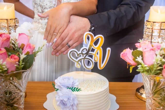 A bride and groom display their wedding rings in front of a wedding cake