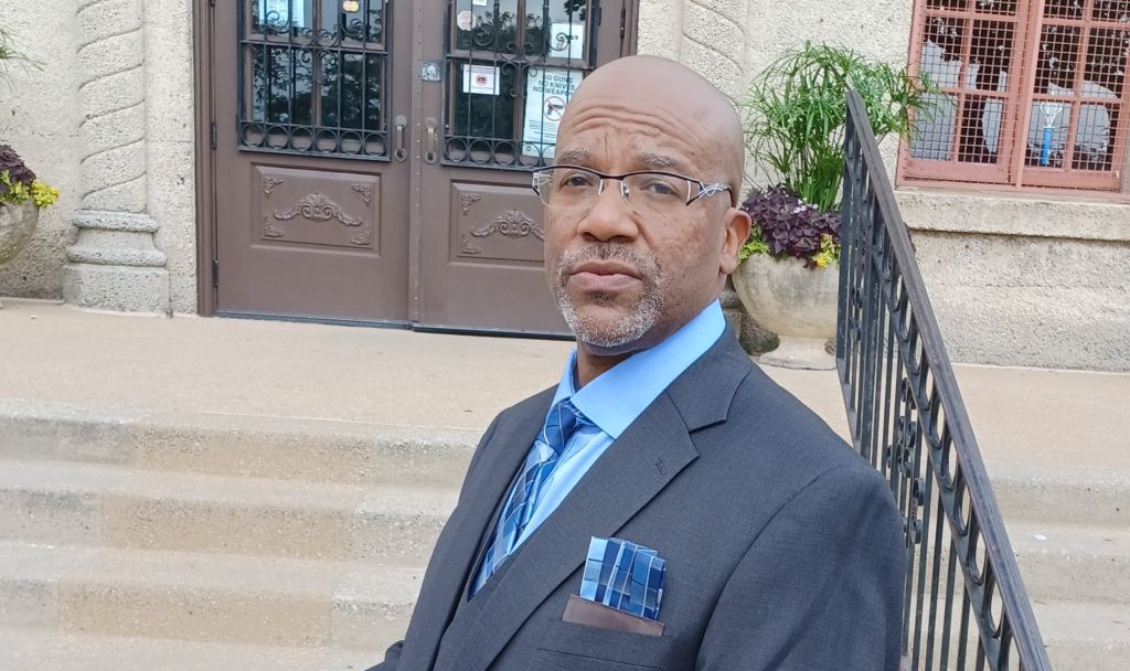 A well dressed groom in a dark grey suit and light blue shirt awaits his marriage ceremony outside a church